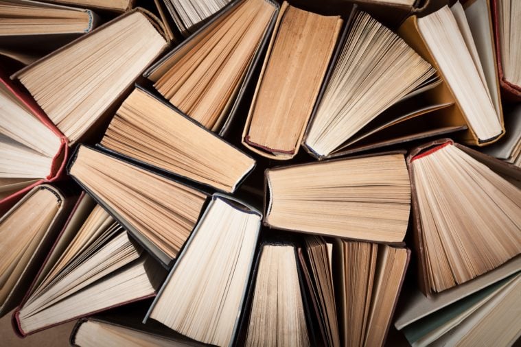 A collection of hardcover books, seen lengthwise from the bottom so their pages, but not their spines are visible. They seem to form a strong wall.