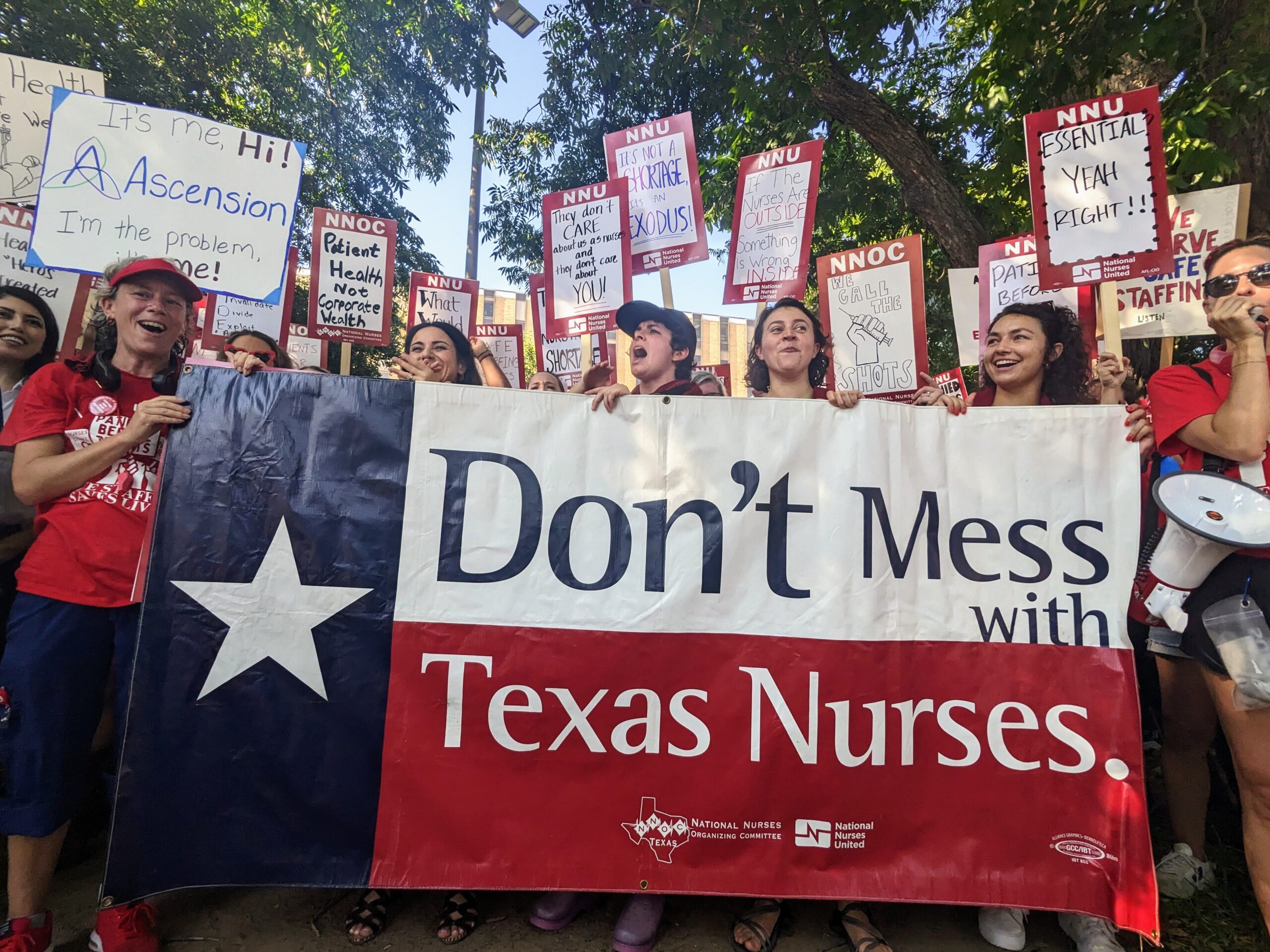 A group if striking nurses hold National Nurses United strike signs and a large banner designed with the Texas flag and the words Don't Mess with Texas Nurses.