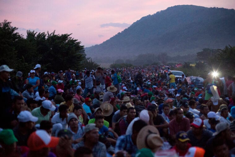 A caravan of Central American migrants huddles together with a mountain in the background